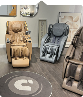 Two massage chairs in a modern showroom, one brown and one gray, with a round logo rug on the floor.