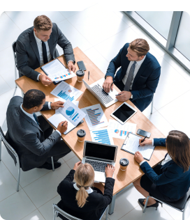 Group of professionals discussing charts and data at a conference table with laptops and coffee cups.